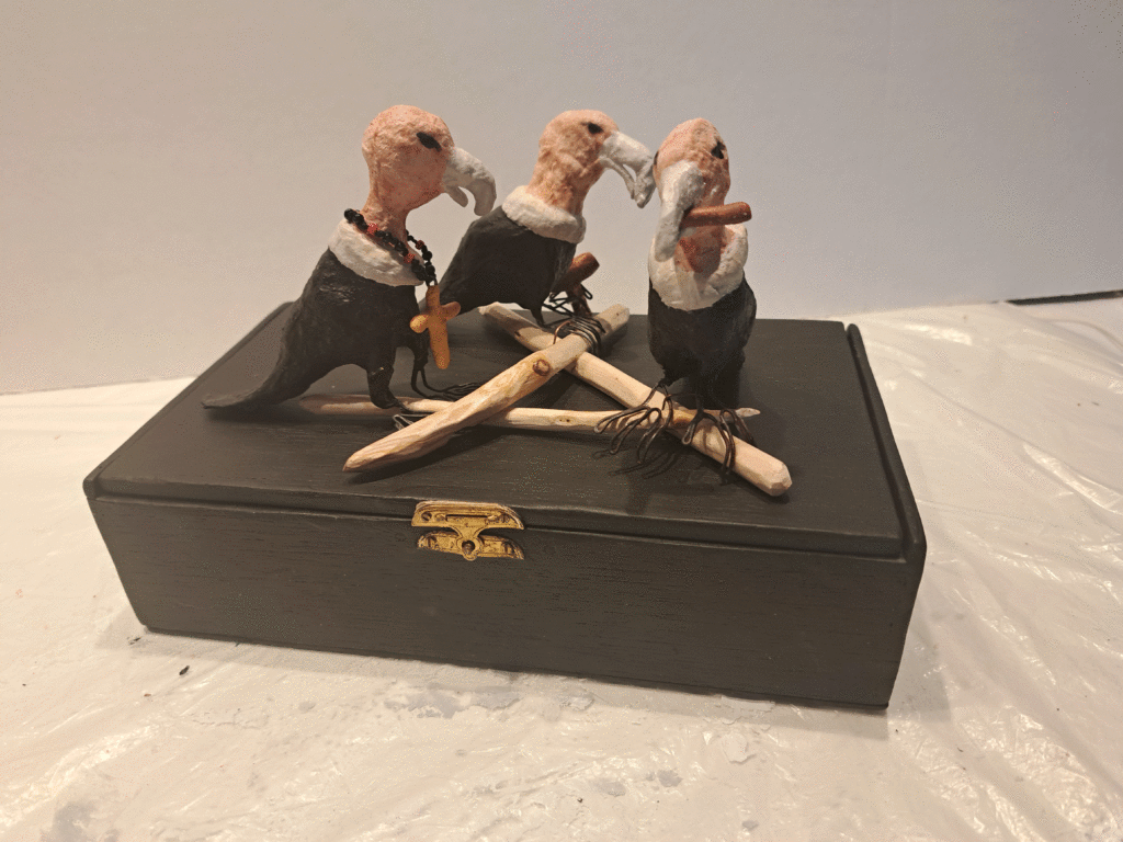 Three vultures--priest, politician, judge--perched on an "A" made of dead, bare branches on top of box lid