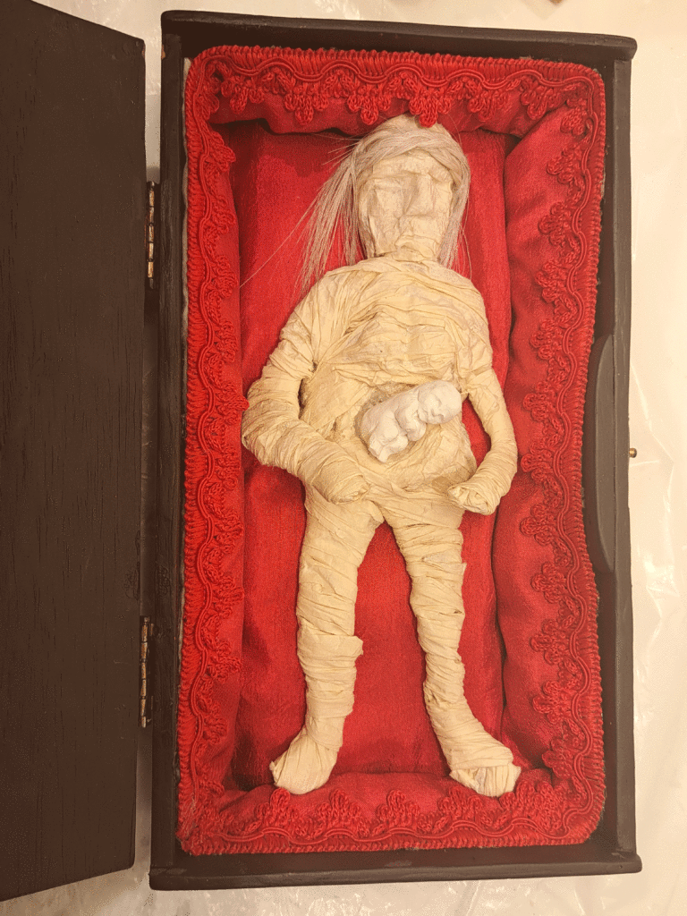 A: Abolition of Abortion=Abolition of Autonomy Mummified woman with perfect, white fetus lying in red-silk lined coffin